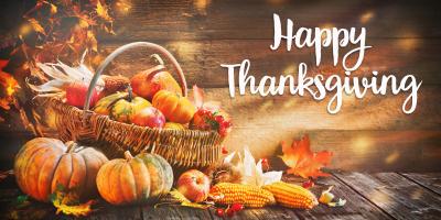 The words Happy Thanksgiving next to a basket overflowing with pumpkins, corn, leaves and fruit